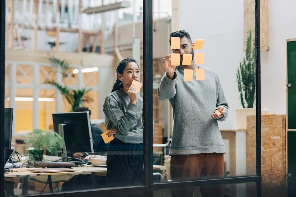 Colleagues collaborating with sticky notes on a glass wall